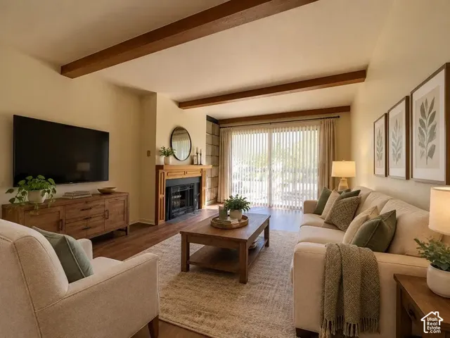 Living area featuring exposed wood ceiling beams, wood-finish flooring, a wood-mantle fireplace with stone surround, and sliding glass doors