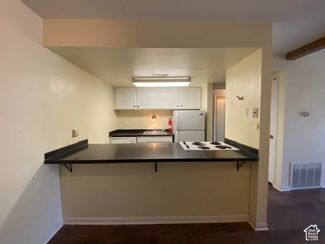 Kitchen featuring an integrated breakfast bar with dark countertops, white cabinetry, built-in cooktop, and wood-finish flooring