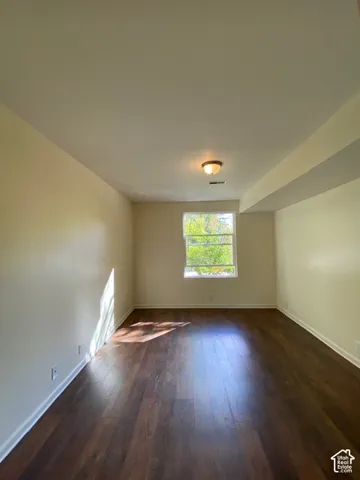 Room featuring dark-toned wood-finish flooring, a central ceiling-mounted light fixture, and a single-pane window
