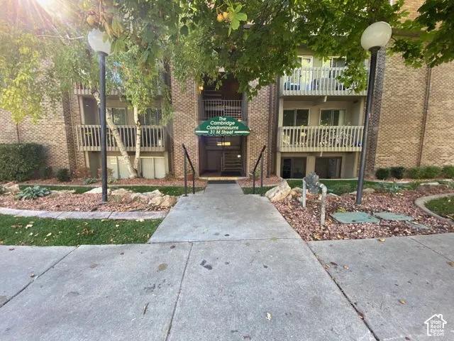 Brick exterior featuring tiered balconies, decorative metal railings, concrete walkways, and post-mounted exterior lighting