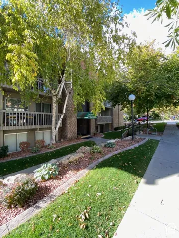 Multi-story brick exterior featuring private balconies with railings, landscaped rock garden beds, mature trees, and concrete walkways