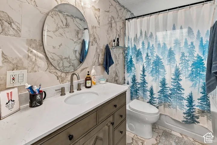 Bathroom featuring a vanity with quartz countertop, under-mount oval sink, circular wall-mounted mirror, and wall-tiling with natural stone-finish