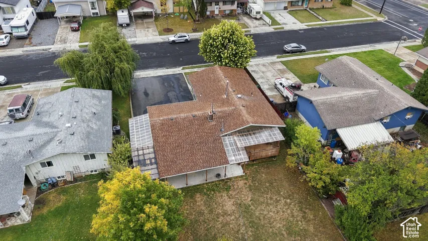 Aerial perspective of residential property featuring an asphalt driveway, covered patio area, mature trees, and a spacious lawn