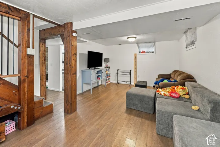 Open-concept room featuring wood-finish flooring, exposed timber support columns, a staircase with metal railings, and dual recessed windows