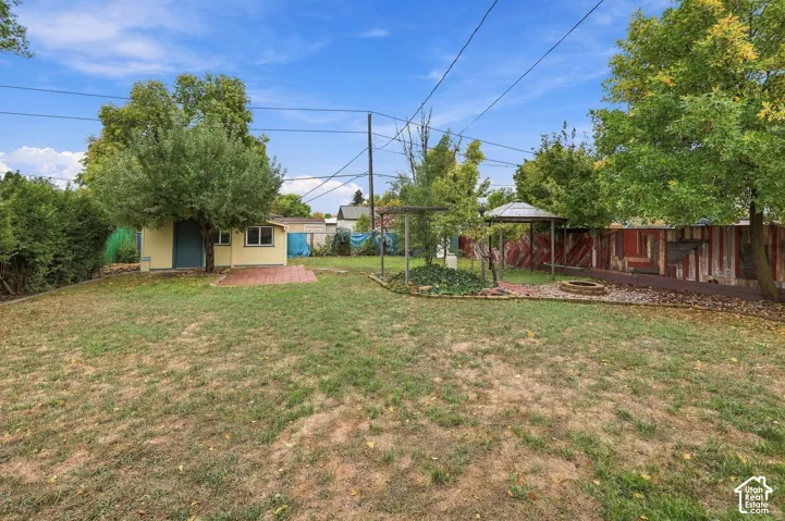 Fenced backyard featuring a detached outbuilding, a brick patio, a wooden arbor, and a gravel fire pit area