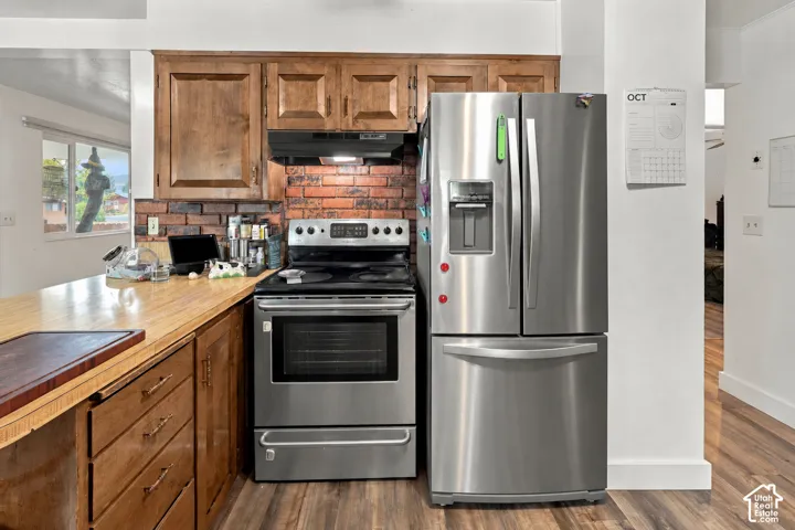 Kitchen featuring custom wood cabinetry, exposed brick backsplash, wood-surface countertop, and stainless steel appliances