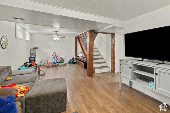 Wood-finish flooring, white painted brick wall, exposed structural timber support beams, and a staircase featuring integrated cabinetry