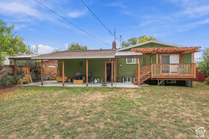 Rear exterior featuring a covered concrete patio, an elevated wooden deck, a wood-slat pergola, and wood privacy fencing