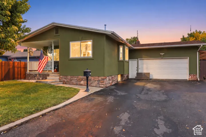 Single-story exterior featuring a stone-veneer foundation, covered front porch, attached garage, and paved driveway