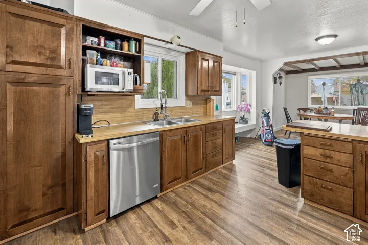 Kitchen featuring stained wood cabinetry, stainless steel dishwasher, wood-finish flooring, built-in recessed lighting, and a bay window