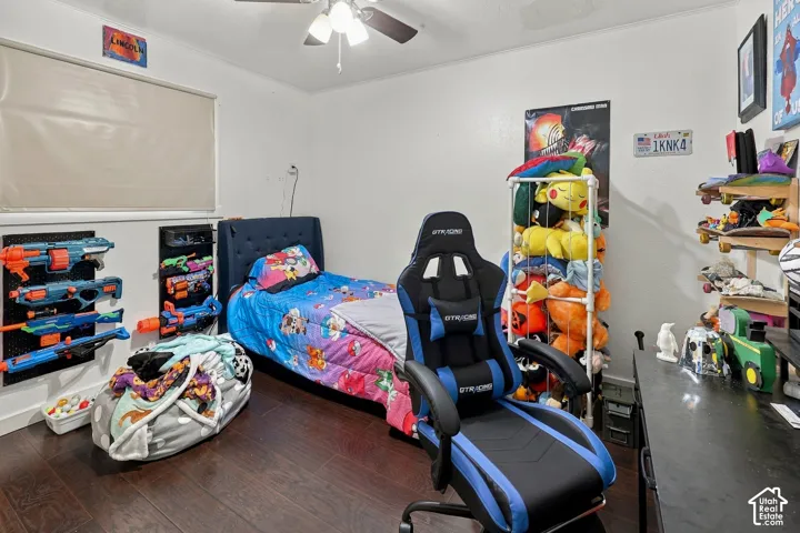 Room featuring dark wood-finish flooring, a wall-mounted roller shade, and a central ceiling fan with an integrated light fixture