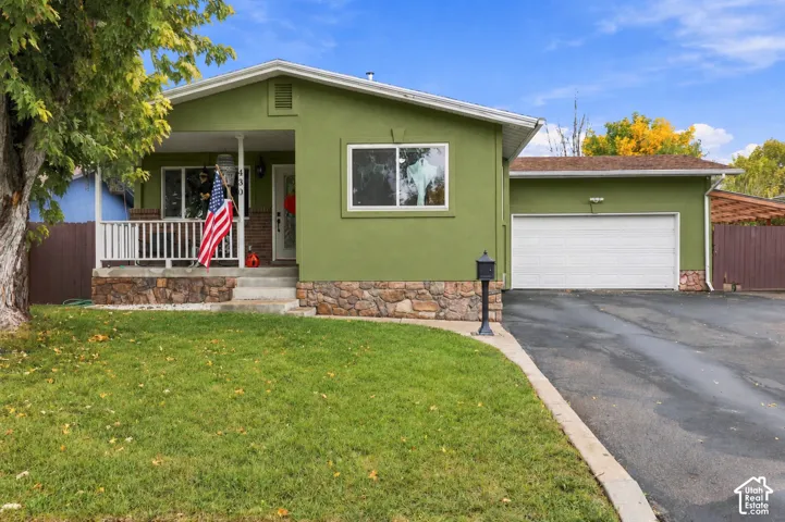 Exterior featuring stucco siding, stone veneer accents, an attached garage, and a covered front porch with a wood-style railing