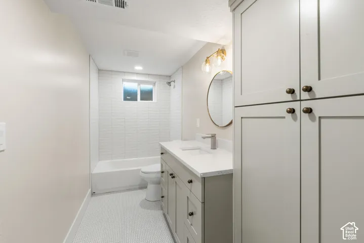 Bathroom featuring white subway tile shower surround, white bathtub, white penny tile flooring, light gray vanity with white countertop, and built-in gray cabinetry