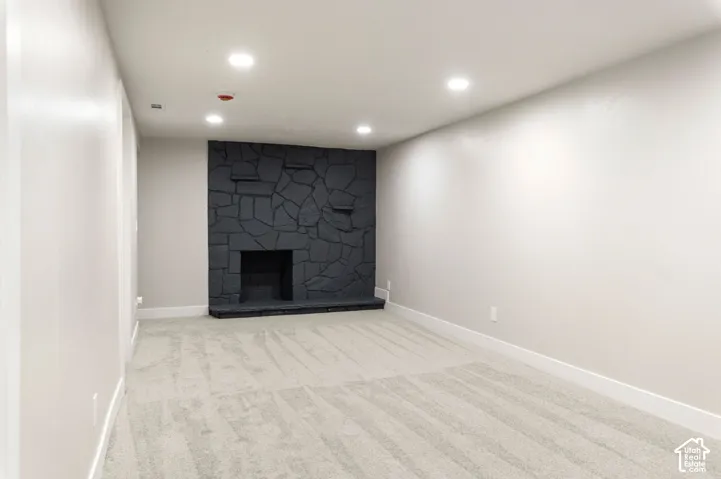 Recessed lighting, light gray carpeting, neutral wall color, dark stone fireplace, and white trim