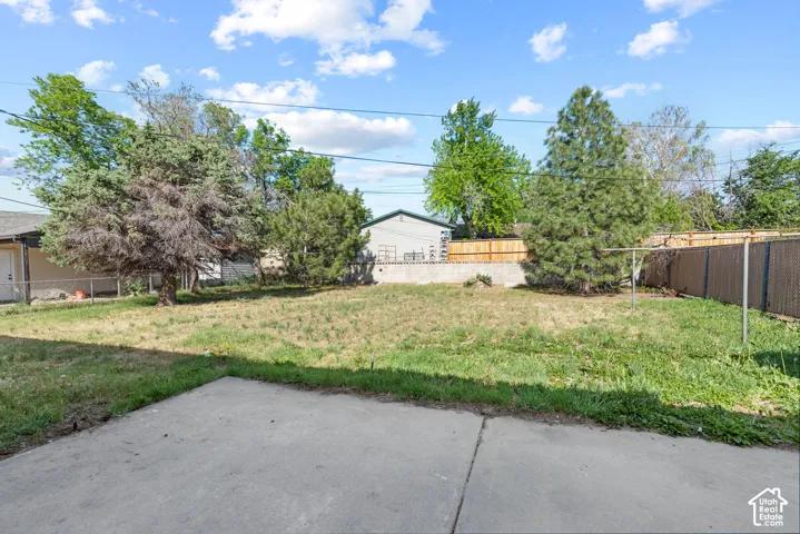 Concrete patio with a spacious yard, mature trees, and a privacy fence