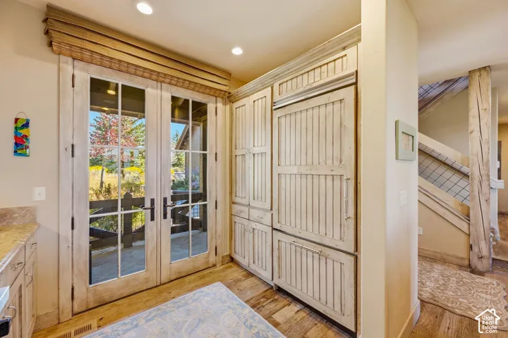 Paneled French doors, distressed-finish built-in cabinetry, integrated refrigerator, and wood-finish flooring