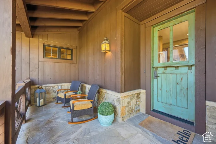 Covered entryway featuring natural stone flooring, vertical wood-plank siding, stone wainscoting, and a painted wood-framed glass entry door