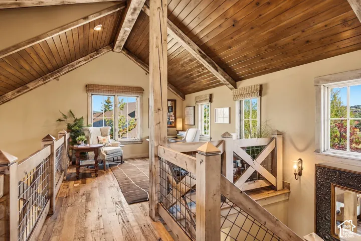 Vaulted ceilings with exposed timber beams and wood-plank paneling, wood-finish flooring, and custom wood railing featuring wire mesh detailing
