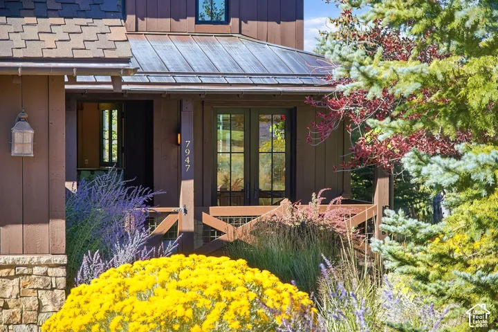 Exterior facade featuring wood board-and-batten siding, a metal standing-seam roof, natural stone base, custom wood porch railing, and double glass-paned doors