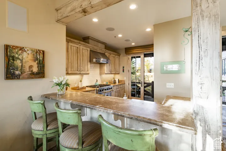 Kitchen featuring stone-surface breakfast bar, wood-finish cabinetry, stainless steel range with overhead hood, and exposed wood structural beam