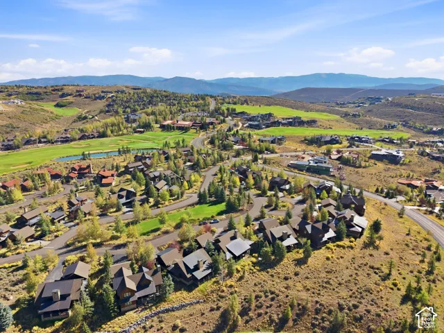 Aerial landscape featuring mountain topography, mature coniferous and deciduous trees, winding paved roads, and open green space