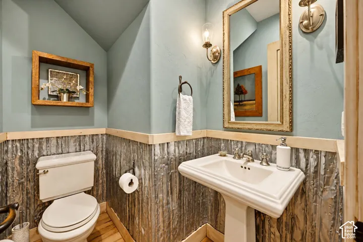 Restroom featuring corrugated metal wainscoting, wood trim, pedestal sink, wall-mounted light fixtures, and wood-finish flooring