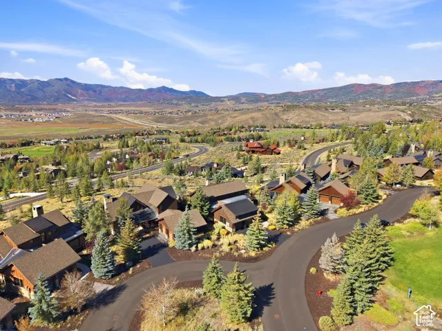 Aerial perspective of a mountain community featuring wood and stone exterior dwellings, paved roadways, mature coniferous landscaping, and a panoramic mountain backdrop