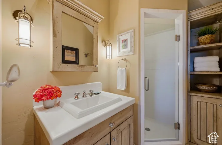 Vanity featuring a farmhouse-style wood cabinet, integrated rectangular sink, wall-mounted light fixtures, and a matching wood-framed mirror, complemented by a glass-enclosed shower and built-in shelving