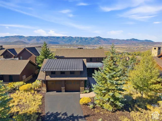 Two-story residence featuring a metal and shingle roof, two-car garage, stone masonry accents, and a paved driveway, set against a prominent mountain backdrop