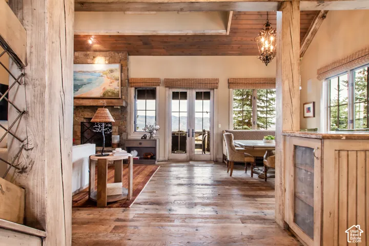 Living area featuring wood-finish flooring, exposed timber support beams, a stone-surround fireplace, a wood-paneled ceiling, and French doors
