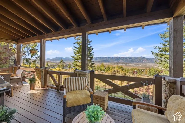 Covered deck featuring wood decking, exposed timber beams, rustic stone pillars, and metal cross-buck railing, highlighting mountain and valley scenery