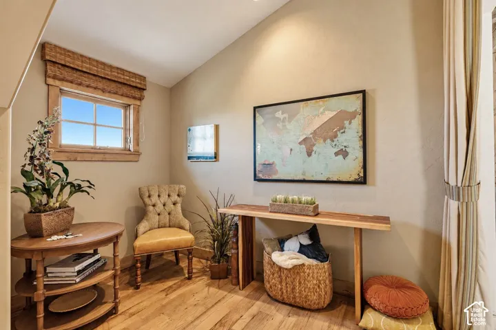 Vaulted ceiling featuring wood-finish flooring, natural wood window trim, and a woven window shade