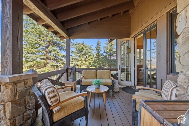 Covered wooden deck featuring natural stone pillar bases, wood-beam ceiling, and multi-pane glass door entry