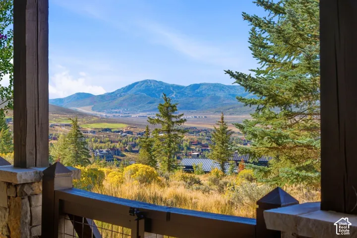 Covered porch with heavy timber posts, stone column bases, and a metal grid railing, showcasing expansive mountain and valley scenery