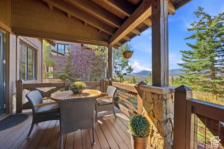 Covered deck featuring wood decking, exposed timber ceiling beams, stone-based columns, and wire-mesh railing, accented by a mountainous landscape