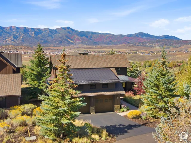 Mountain residence with metal and shingle roofing, wood siding, stone base accents, and an attached multi-car garage, featuring expansive mountainous scenery
