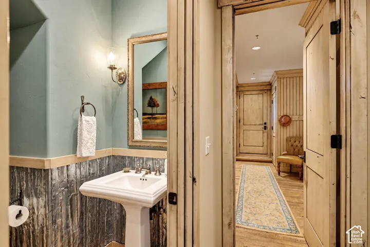 Powder room featuring a pedestal sink, textured metal wainscoting, and wall-mounted light fixture, accented by rustic wood-paneled door casing and trim