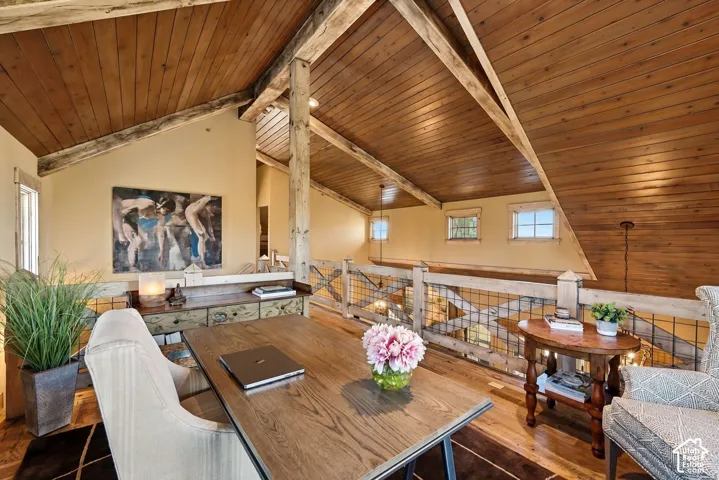 Vaulted ceilings with exposed timber beams and tongue-and-groove wood paneling, wood-finish flooring, and a decorative metal-mesh balcony railing