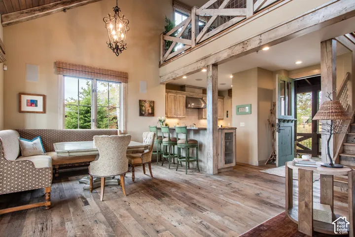 Vaulted ceilings with exposed timber beams, wood-finish flooring, custom cabinetry, decorative wrought-iron chandelier, and elevated mezzanine with rustic railing