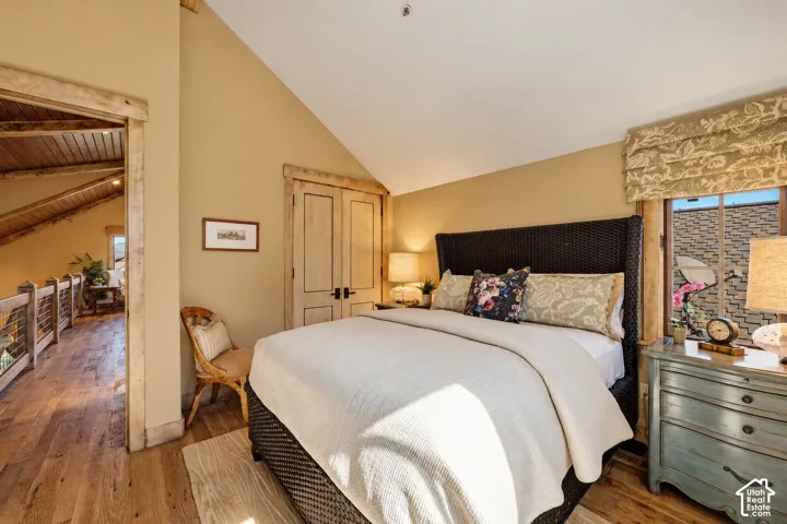 Vaulted ceiling featuring wooden beam accents, wood-finish flooring, and natural wood door casings