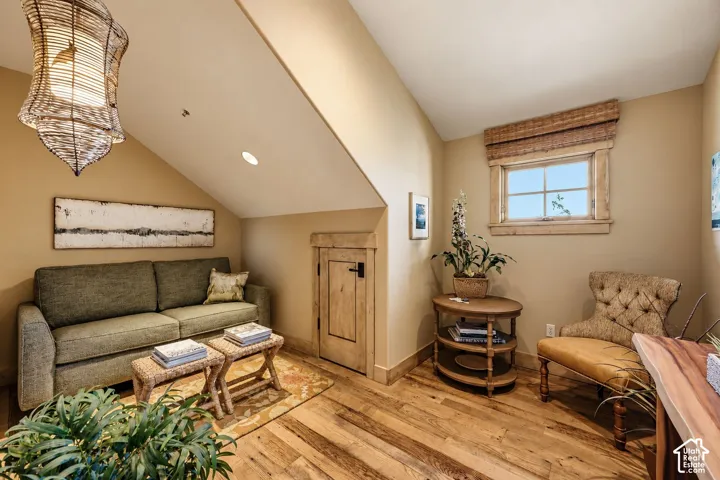 Sloped ceiling with recessed lighting, wood-finish flooring, built-in lower-level storage access door with wood trim, and a window with custom wood casing