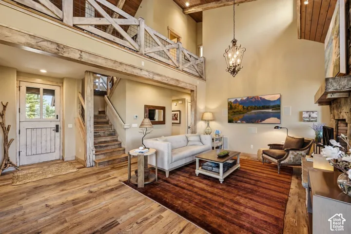 Double-height living area featuring exposed wood ceiling beams, a wood-trimmed mezzanine with a rustic railing, wood-finish flooring, and a stone-clad fireplace