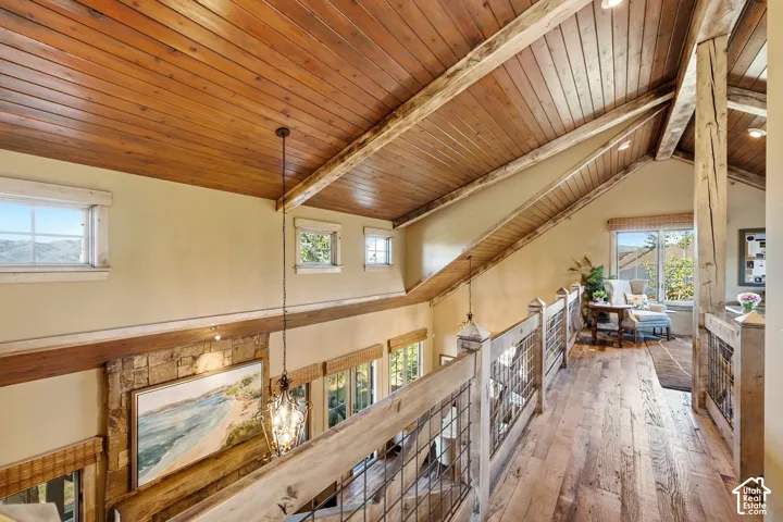 Vaulted ceiling with tongue-and-groove wood paneling, exposed structural timber beams, wood-finish flooring, and railing featuring natural wood posts with wire mesh inserts