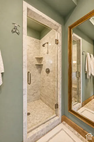 Walk-in shower featuring a frameless glass door, stone-tile surround, built-in corner shelving, and polished chrome plumbing fixtures