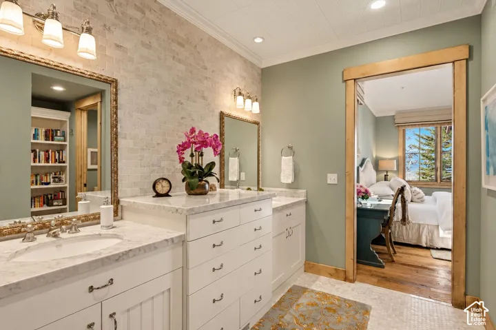 Bathroom vanity featuring white cabinetry, stone-finish countertops, dual under-mount sinks, and a textured stone-tile backsplash