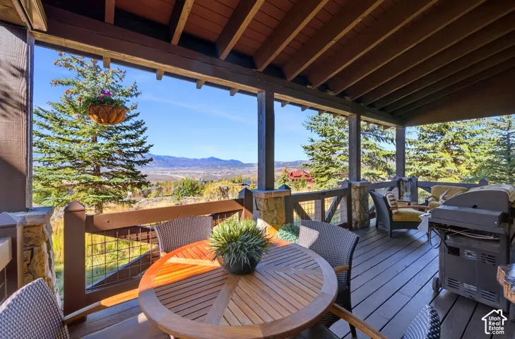 Covered deck featuring wood-finish decking, exposed beam ceiling, stone pillar accents, and wire railing