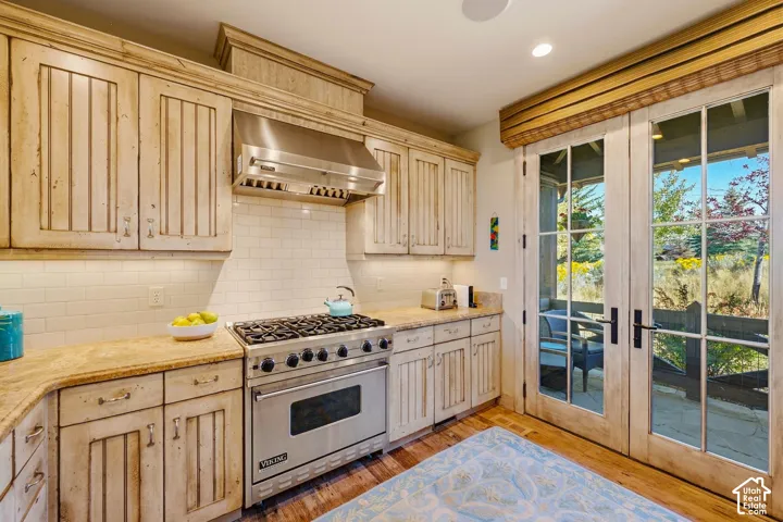 Distressed-finish custom cabinetry, stainless steel professional-grade range with matching hood, stone countertops, white subway tile backsplash, and full-glass French doors