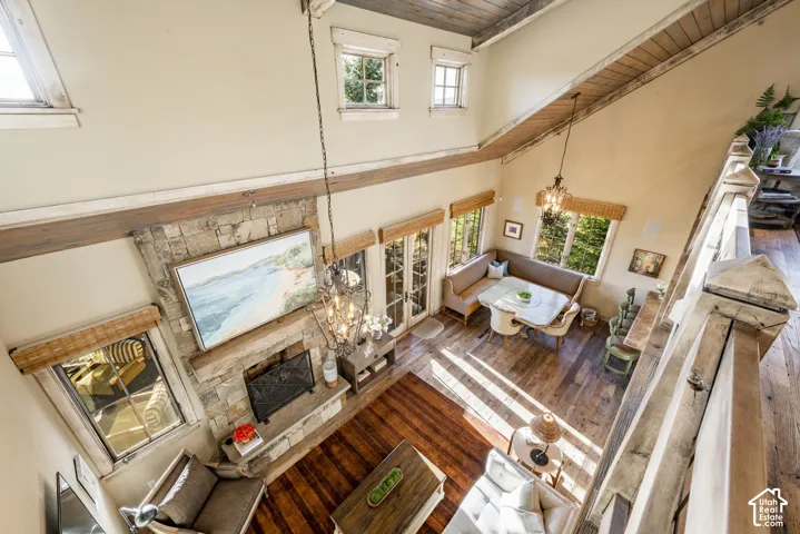 Vaulted ceilings with exposed timber beams, stacked stone fireplace, wood-finish flooring, multi-pane windows, and wrought iron chandelier