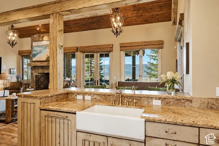 Stone countertop with an integrated apron-front sink, rustic timber support post, wood-planked ceiling, and a floor-to-ceiling stone fireplace