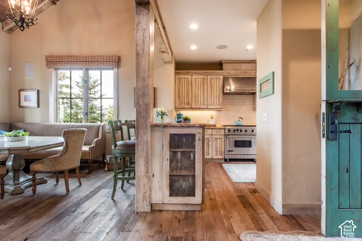 Vaulted ceiling with exposed wood beam, wood-finish flooring, custom cabinetry, stainless steel professional-grade range, and built-in glass-front display cabinet
